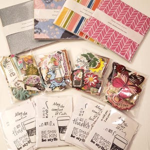 May include: A collection of colorful paper packs and decorative embellishments for scrapbooking and crafting. The paper packs feature various patterns and colors, including pink, blue, and green. The embellishments include butterflies, flowers, and other decorative elements. The text on the paper packs reads "Dream Create Inspire" and "Dream Create".