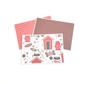 May include: A collection of patterned paper sheets featuring dog-themed designs. One sheet has a red polka dot pattern, another has a brown dotted pattern, and the third has a repeating pattern of dog houses, bones, and paw prints.