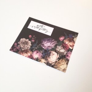 May include: A sympathy card with a dark background and a floral design featuring pink, purple, and cream-colored flowers. The card has the words "with sympathy" in a white rectangle.
