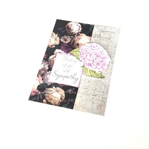 May include: A sympathy card with a floral design. The card features a dark background with roses and a light pink hydrangea. The text "Thinking of you with Sympathy" is displayed in a white frame.