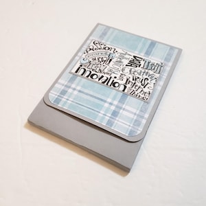 May include: A gray notebook with a light blue plaid design on the cover. The cover has a rectangular label with the words "passion, innovation, communicate, be real, team, work, creative, trust, internet, things" in a black and white design.