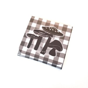 May include: A square notepad with a black and white checkered pattern. The notepad features a sticker with four black mushroom illustrations. The mushrooms have detailed caps and stems, with one mushroom having white spots.