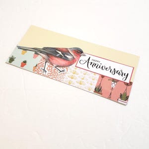 May include: An anniversary card featuring a watercolor illustration of a red and gray bird perched on a patterned background. The card has the words "Happy Anniversary" in elegant script.