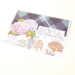 May include: A greeting card with a watercolor design. The card features pink and purple hydrangeas, green leaves, and the words "Get Well Soon." The background has a plaid pattern and decorative floral elements.