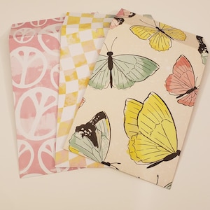 May include: Three decorative envelopes with different patterns. One envelope has a pink background with white peace signs, another has a yellow and white checkered pattern, and the third has a cream background with a watercolor butterfly pattern.