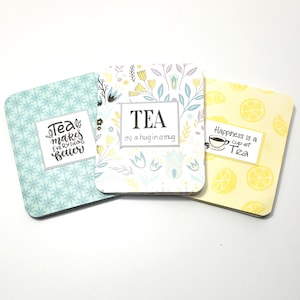 May include: Three decorative tea-themed coasters. One is light blue with a floral pattern and the text "Tea makes everything better." Another is white with floral designs and the word "TEA." The third is yellow with lemon slices and the text "Happiness is a cup of Tea."