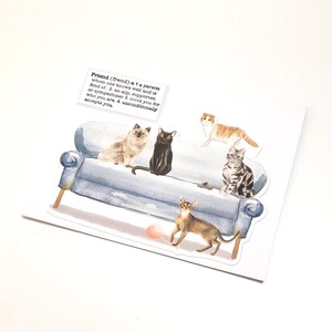 May include: A greeting card featuring a watercolor illustration of a blue sofa with six different cat breeds. The cats are in various poses. A small text box above the sofa defines the word "Friend".
