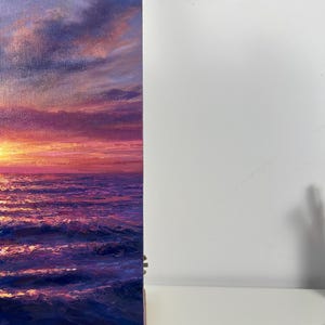 May include: An oil painting depicts a vibrant sunset over the ocean. The sky transitions from deep blue to shades of pink and orange, reflecting on the water's surface. The artwork captures the dynamic interplay of light and water.