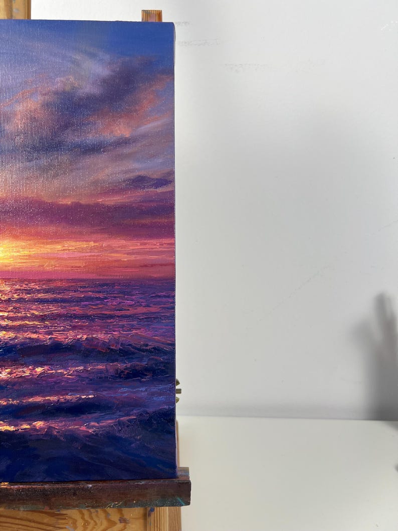 May include: An oil painting depicts a vibrant sunset over the ocean. The sky transitions from deep blue to shades of pink and orange, reflecting on the water's surface. The artwork captures the dynamic interplay of light and water.