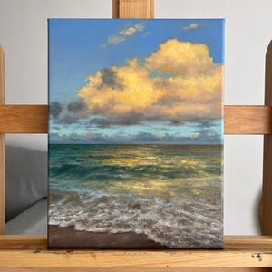 Puede incluir: Una pintura al óleo sobre lienzo que representa un paisaje marino al atardecer. La escena muestra un cielo azul brillante con grandes nubes de color amarillo dorado sobre un océano verde oscuro con espuma blanca en una playa de arena marrón.