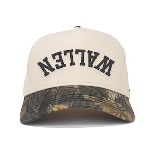 Peut inclure: Casquette de baseball beige avec le mot "WALLEN" en lettres noires sur le devant. La visière présente un motif camouflage dans les tons de marron, vert et noir. La casquette a une visière incurvée et une couronne structurée.