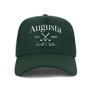 Può includere: Cappellino da baseball verde scuro con visiera curva. Presenta la scritta bianca "Augusta Golf Club", mazze da golf incrociate e l'anno "1993". Un accessorio classico per gli appassionati di golf.