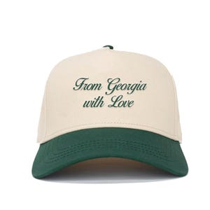 Op de afbeelding: Een baseballpet met een crèmekleurige kroon en een donkergroene klep. De tekst "From Georgia with Love" is in een scriptletter op de voorkant geborduurd. De pet heeft een gebogen klep en een donkergroene knop bovenop.