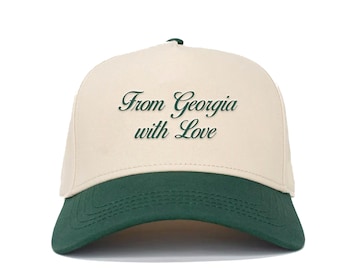 Könnte beinhalten: Baseballcap mit cremefarbener Krone und dunkelgrünem Schirm. Der Text "From Georgia with Love" ist in einer Schriftart auf der Vorderseite gestickt. Die Kappe hat einen gebogenen Schirm und einen dunkelgrünen Knopf oben.