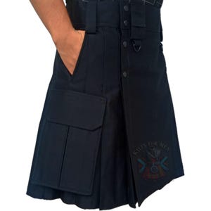 Peut inclure: Un kilt utilitaire noir doté d'une large ceinture avec passants, d'une fermeture à boutons sur le devant et de grandes poches cargo latérales. Le vêtement comprend un anneau en D et un écusson circulaire avec le texte KILTS FOR MEN.