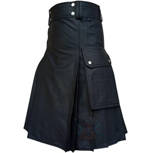 K&ouml;nnte beinhalten: Ein schwarzer Utility-Kilt mit einem breiten Bund, zwei silberfarbenen Metalldruckkn&ouml;pfen, vertikalen Falten und einer gro&szlig;en, rechteckigen Cargotasche an der Seite, die mit einem silberfarbenen Druckknopf verschlossen wird. Das Kleidungsst&uuml;ck hat eine glatte, matte Oberfl&auml;che.