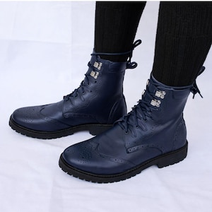May include: A pair of navy blue leather ankle boots with brogue detailing. The boots have a lace-up closure, silver-tone hardware, and a rounded toe. The soles are black, and the boots are worn with black socks.