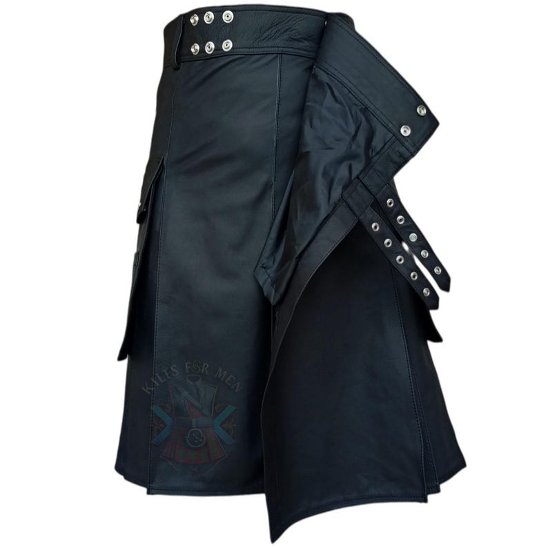 K&ouml;nnte beinhalten: Ein schwarzer Lederkilt im Wickeldesign mit mehreren silberfarbenen Metalldruckkn&ouml;pfen am Bund und an der Seite. Das Kleidungsst&uuml;ck verf&uuml;gt &uuml;ber seitliche Cargotaschen und verstellbare Riemen mit Metall&ouml;sen. Ein Logo ist auf der Vorderseite sichtbar.