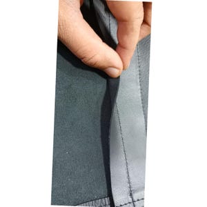 K&ouml;nnte beinhalten: Ein St&uuml;ck dunkelgraues Material mit einer glatten, bearbeiteten Au&szlig;enseite und einer texturierten, matten Unterseite. Das Material weist eine gerade, verst&auml;rkte Naht auf, die vertikal entlang der Kante verl&auml;uft und den Kontrast zwischen beiden Seiten zeigt.