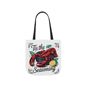May include: White tote bag with a red lobster in a blue bowl and a lemon slice. The text "Tis the Seasoning" is printed on the bag.