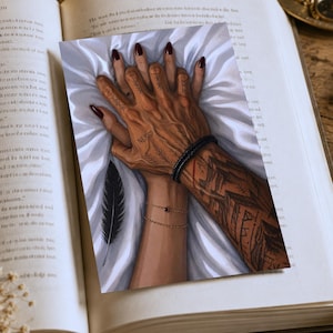 Może przedstawiać: Ilustracja dw&oacute;ch splecionych dłoni, z kt&oacute;rych jedna ma skomplikowane tatuaże i czarną bransoletkę, a druga delikatną złotą bransoletkę. Paznokcie pomalowane są na głęboki czerwony kolor. W pobliżu leży czarne pi&oacute;ro.
