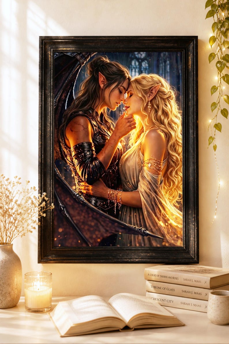 May include: A framed art print depicts two figures in an embrace, with one figure having dark wings. The artwork features a fantasy theme with soft lighting and a detailed background. The frame is black, and the print is displayed on a white surface with books and a candle.