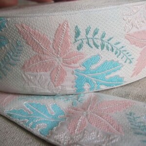 Puede incluir: Cinta blanca con un estampado floral de hojas y ramitas rosas y turquesas. La cinta está enrollada, con una parte desenrollada, mostrando el diseño repetitivo. La cinta tiene un aspecto texturizado.
