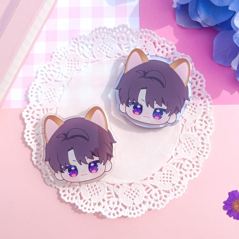 Peut inclure: Deux breloques en acrylique transparent repr&eacute;sentant un personnage de dessin anim&eacute; aux cheveux violets et aux oreilles de chat. Le personnage a les yeux violets et un petit sourire. Les breloques sont sur une nappe en dentelle blanche, avec un fond &agrave; carreaux roses et blancs.