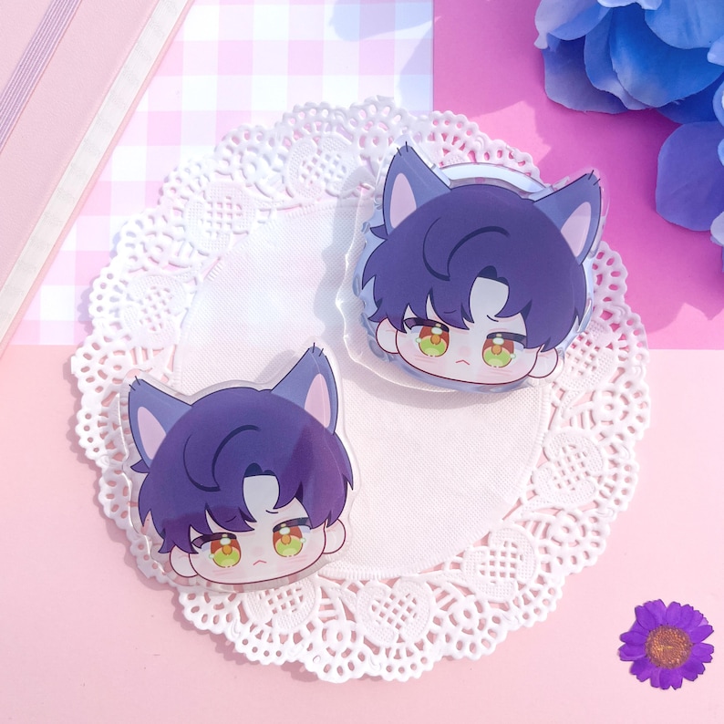 Peut inclure: Deux breloques en acrylique transparent repr&eacute;sentant un personnage de dessin anim&eacute; aux cheveux violets et aux oreilles de chat. Le personnage a les yeux verts, pos&eacute; sur une nappe en dentelle blanche sur fond rose. Une fleur violette et des accents floraux bleus sont &eacute;galement visibles.