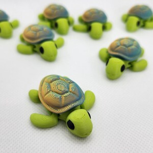Peut inclure: Un groupe de sept petites tortues de mer imprimées en 3D, de couleur verte et bleue. Les tortues ont une carapace texturée et des yeux noirs.