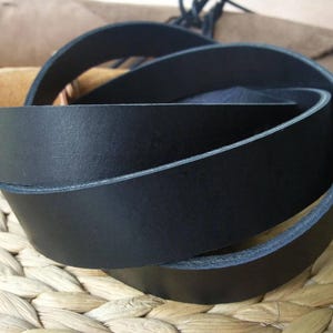 May include: A coiled black leather belt, showcasing a smooth, dark surface. The edges are neatly finished, and the belt appears to be of high quality. The background features natural textures, suggesting a focus on craftsmanship and natural materials.