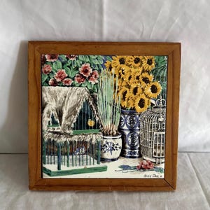 May include: A framed ceramic tile with a still life design. The image shows birdcages, sunflowers, and plants in vases. The frame is made of wood. The colour scheme includes green, yellow, blue, and brown.