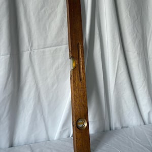 May include: A vintage wooden level, rectangular in shape, with a dark brown finish. It features two bubble vials for measuring levelness, encased in clear glass and filled with yellow liquid. This carpentry tool measures approximately 60 cm in length.