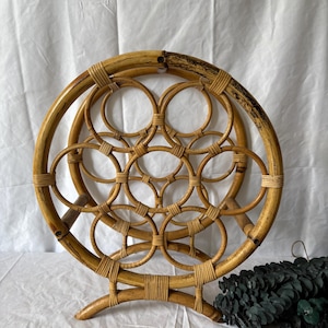 Peut inclure: Un porte-bouteilles rond en rotin de couleur naturelle. Le porte-bouteilles présente un design circulaire avec des anneaux entrelacés et une base pour la stabilité. Il est fait de rotin brun clair et présente un motif tissé.