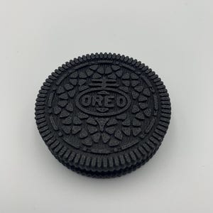 May include: A black Oreo cookie with the brand name embossed on the top cookie. The cookie has a detailed, textured pattern around the edges and on the surface.