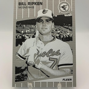 May include: A grayscale baseball card featuring Bill Ripken, a second baseman. The card displays the player in his Orioles uniform, holding a bat. The card has the text "Bill Ripken, Second Base" and the Fleer logo.