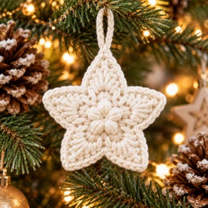 May include: A cream-colored, five-pointed star ornament crafted from thick yarn using a crochet technique. The star features a central flower-like cluster of stitches and a braided loop at the top for hanging, showcasing a textured, handmade appearance.