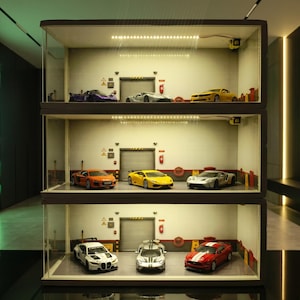 May include: A three-tiered display case showcasing miniature model cars. Each level features a different car, including a purple sports car, a silver coupe, and a yellow Camaro. The display case has a garage-like backdrop with overhead lighting.
