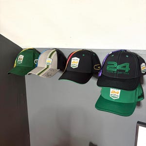 May include: Five baseball caps with green, black, and grey brims and white, yellow, and purple accents. The caps have the text "Rolex 24 Hours at Daytona" on them.