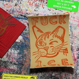 May include: Tan fabric patch with an orange cat graphic and the word "FUCK". Below the cat is the text "I.C.E.". A green sticker reads "FIRST 20 ORDERS GET 1 OF 2 BONUS PATCHES". A yellow sticker says "FEED THE STRAYS REALLY MEANS FEEDING THE STRAYS."