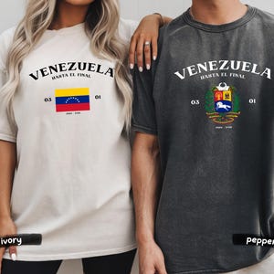 May include: Two t-shirts, one ivory and one pepper, featuring the word "VENEZUELA" above the phrase "HASTA EL FINAL." Each shirt displays a Venezuelan flag or coat of arms, along with the numbers "03" and "01."