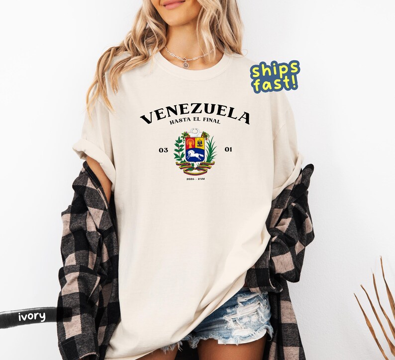 May include: Ivory-colored t-shirt featuring the word "VENEZUELA" above a coat of arms design. The coat of arms includes a horse, wheat, and other symbols. The text "HASTA EL FINAL" is above the coat of arms.