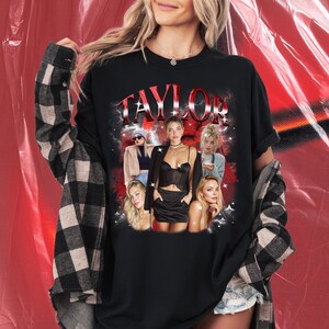 May include: Black t-shirt with the name "TAYLOR" in red, featuring a collage of women. The shirt is worn with a black and white plaid flannel shirt. The background is red.