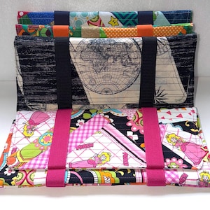 May include: A colorful fabric wallet with multiple compartments. The wallet features a world map design, a black and white pattern, and a pink Princess Peach design. It has black and pink straps.