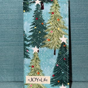 May include: A rectangular quilted fabric case featuring a light blue background with a pattern of green Christmas trees, white stars, and colorful dots. A small rectangular label with the text nJOYnLife is stitched onto the lower front.