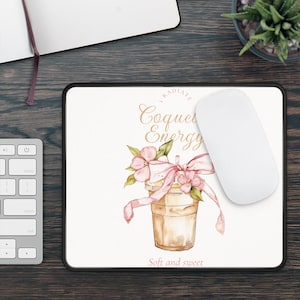 Puede incluir: Alfombrilla de ratón blanca con borde negro. Presenta una ilustración en acuarela de una taza de café con flores rosas y una cinta. El texto "I Radiate Coquet Energy" y "Soft and sweet" también está en la alfombrilla.
