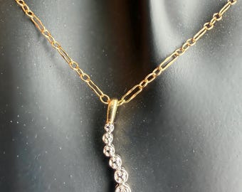 May include: A gold chain necklace featuring a curved pendant set with seven round, clear stones arranged in a vertical, slightly S-shaped line. The chain consists of alternating long and short oval links, connecting to the top of the pendant.