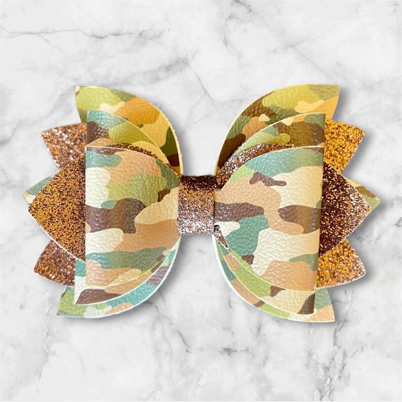 Pu&ograve; includere: Un fiocco per capelli fatto a mano con un motivo mimetico nei toni del verde, marrone e beige. Il fiocco ha un accento dorato glitterato e un nodo centrale abbinato. Questo accessorio &egrave; perfetto per aggiungere un tocco di stile a qualsiasi acconciatura.