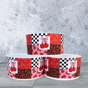May include: Three decorative bowls with a vibrant cherry and bow design. The bowls feature a patchwork pattern with red, pink, and black and white checkered sections. The design includes cherries, bows, and leopard print.