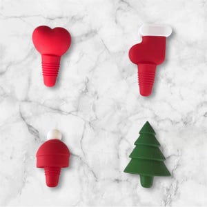 May include: Four festive wine bottle stoppers. The stoppers are red and green, with shapes including a heart, stocking, hat, and Christmas tree. The stoppers are made of a flexible material and have a ribbed design for a secure fit.